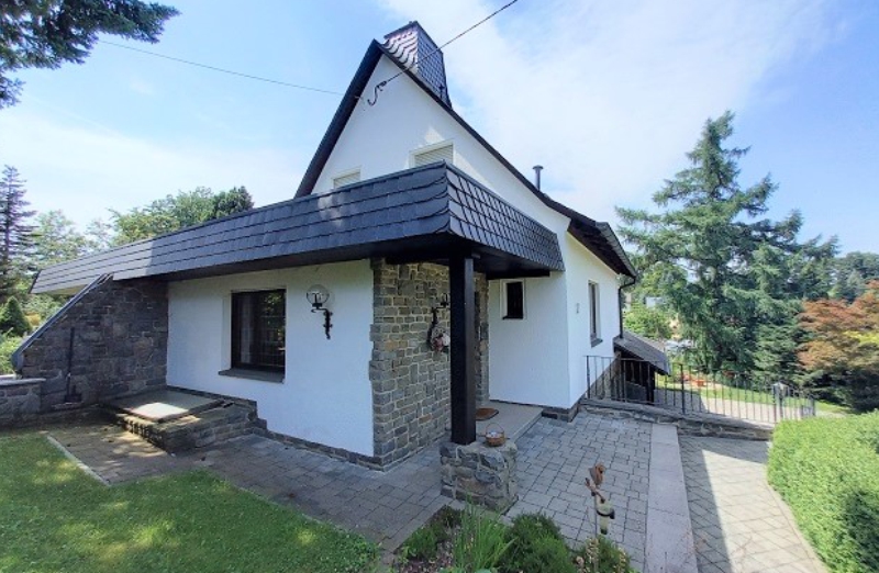 Dieses Bild zeigt ein weißes Einfamilienhaus an einem hellen Tag unter blauem, bewölktem Himmel.