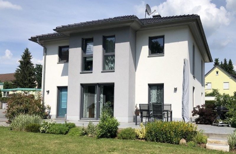 Dieses Bild zeigt ein weißes Einfamilienhaus an einem hellen Tag unter blauem, bewölktem Himmel.