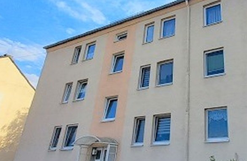 Dieses Bild zeigt ein oranges Etagenwohnhaus in Auerbach an einem hellen Tag unter blauem, bewölktem Himmel.