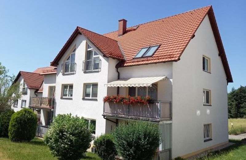 Dieses Bild zeigt ein weißes Etagenwohnhaus mit Balkonen in Burgstädt an einem hellen Tag unter blauem Himmel.