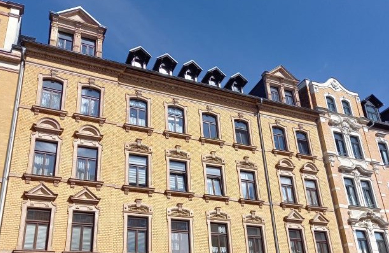 Das Bild zeigt ein gelbes Etagenwohnhaus in Chemnitz an einem hellen Tag unter klarem, blauem Himmel.