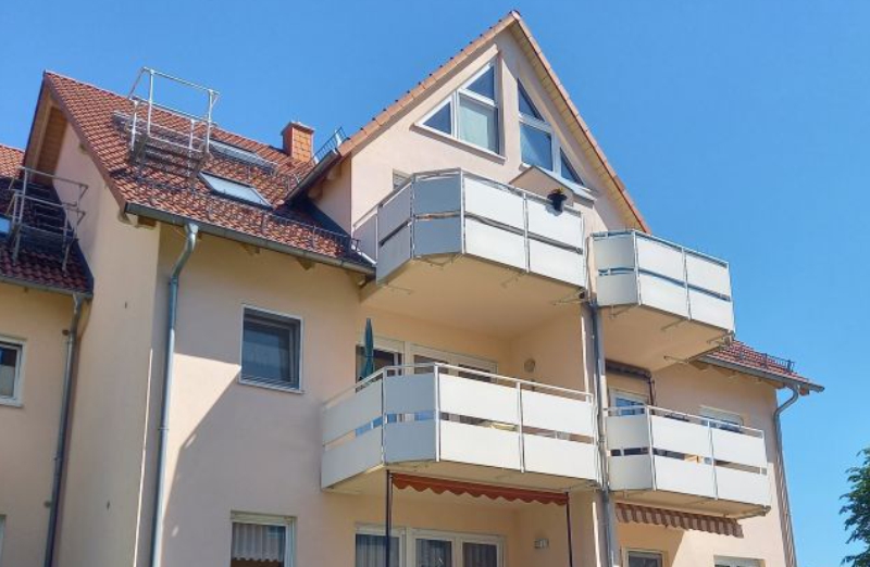 Das Bild zeigt ein oranges Etagenwohnhaus mit Balkonen an einem hellen Tag unter klarem, blauem Himmel.