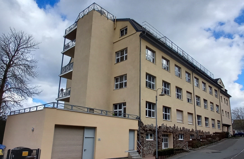 Dieses Bild zeigt ein gelbes Etagenwohnhaus mit Balkonen unter blauem, bewölktem Himmel.