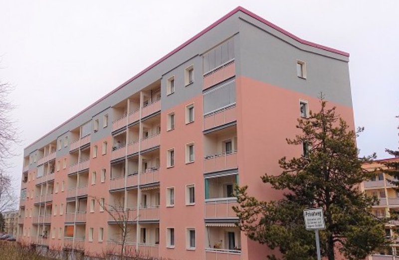 Dieses Bild zeigt ein rotes Etagenwohnhaus mit Balkonen unter bewölktem Himmel.