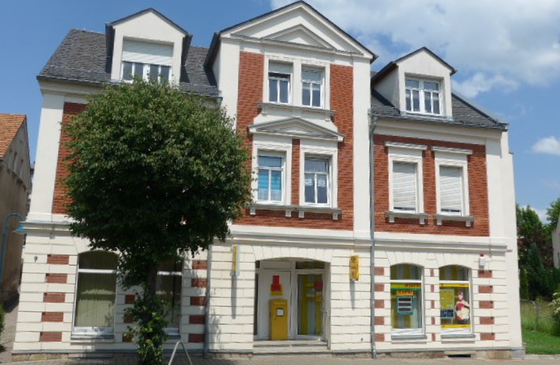 Dieses Bild zeigt ein Mehrfamilienhaus in Oelsnitz an einem hellen Tag unter blauem, bewölktem Himmel.