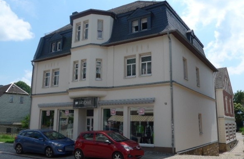 Dieses Bild zeigt ein weißes Mehrfamilienhaus in Oelsnitz an einem hellen Tag unter blauem, bewölktem Himmel.