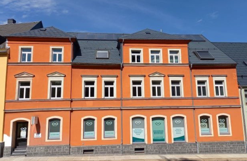 Dieses Bild zeigt ein oranges Mehrfamilienhaus in Thum an einem hellen Tag unter klarem, blauem Himmel.
