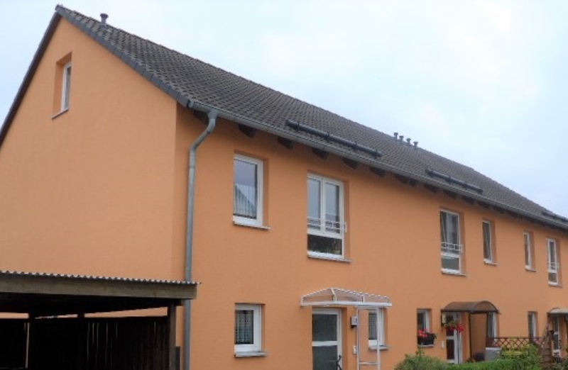 Dieses Bild zeigt ein oranges Reihenhaus in Seifersdorf unter bewölkem Himmel.