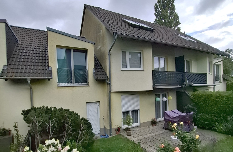 Dieses Bild zeigt ein gelbes Reihenmittelhaus mit Balkon und Garten in Röhrsdorf unter bewölktem Himmel.