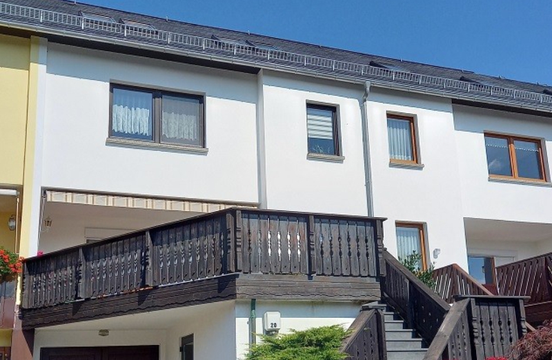 Dieses Bild zeigt ein weißes Reihenmittelhaus mit Balkon in Zschopau an einem hellen Tag unter klarem, blauem Himmel.
