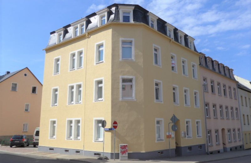 Dieses Bild zeigt ein gelbes Etagenwohnhaus in Mittweida an einem hellen Tag unter blauem, bewölktem Himmel.