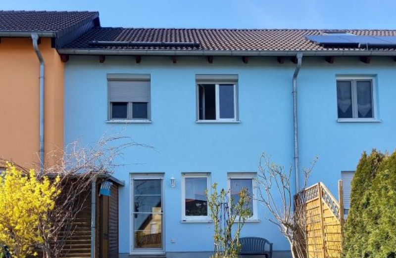Dieses Bild zeigt ein blaues Reihenmittelhaus in Seifersdorf an einem hellen Tag unter klarem, blauem Himmel.